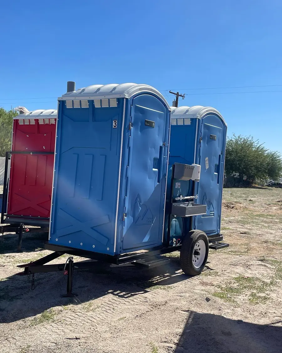 Blue and red portable toilets on a transport trailer in a dry field