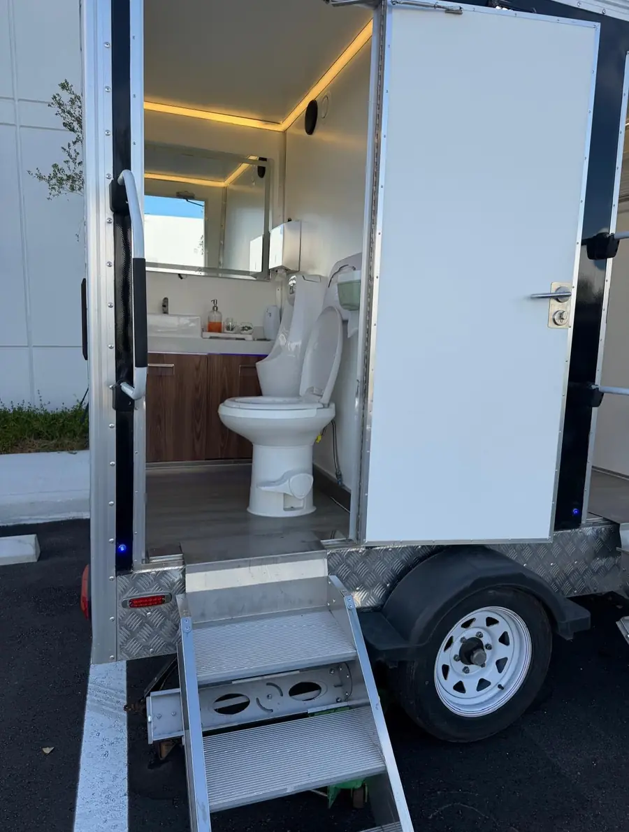 Inside a restroom trailer with a flush toilet and wood vanity
